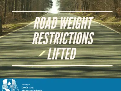 Paved road with trees on both sides, text reads Road Weight Restrictions Lifted